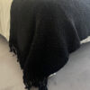 Full black wool throw covering a bed, showing its size and weight.