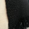 Detail of black wool throw draped over a light couch, focusing on the weave and fringe.