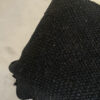 Black wool throw over the edge of a light-colored bed, showing the full woven structure.