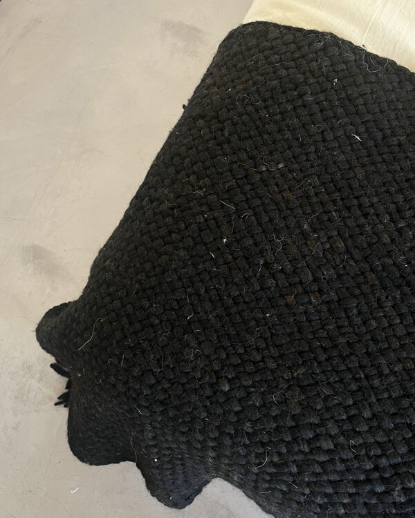 Thick, handwoven black wool throw made from natural sheep's wool, draped over a light-colored surface.