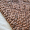 Close-up of the chocolate brown wool throw’s weave lying flat on a bed.