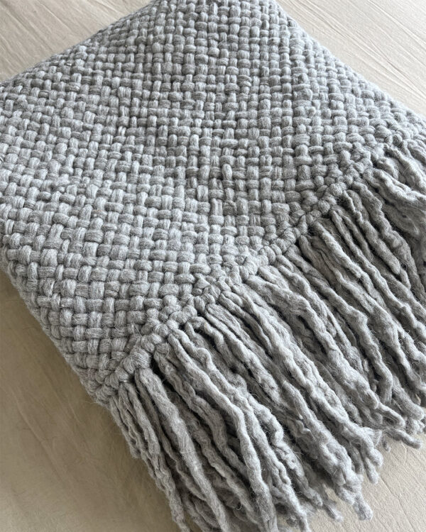 Close-up of a handwoven gray wool throw made from natural sheep's wool, showcasing a thick, textured weave.