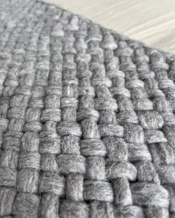 Close-up of a handwoven gray wool throw made from natural sheep's wool, showcasing a thick, textured weave.