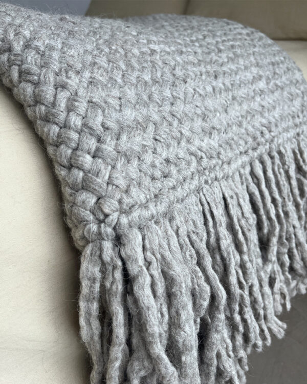 Close-up of a handwoven gray wool throw made from natural sheep's wool, showcasing a thick, textured weave.