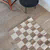 Top view of a sand and natural checkered rug on light wood flooring, next to a small black table.