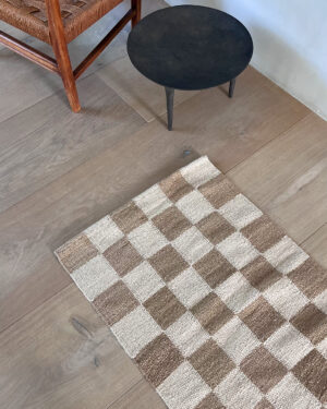 Top view of a sand and natural checkered rug on light wood flooring, next to a small black table.