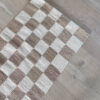 Close-up of a sand and natural checkered rug on light wood flooring, showing the detail of the checkered pattern.