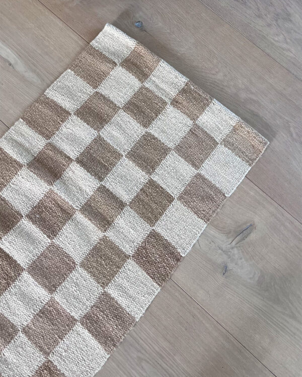 Close-up of a sand and natural checkered rug on light wood flooring, showing the detail of the checkered pattern.