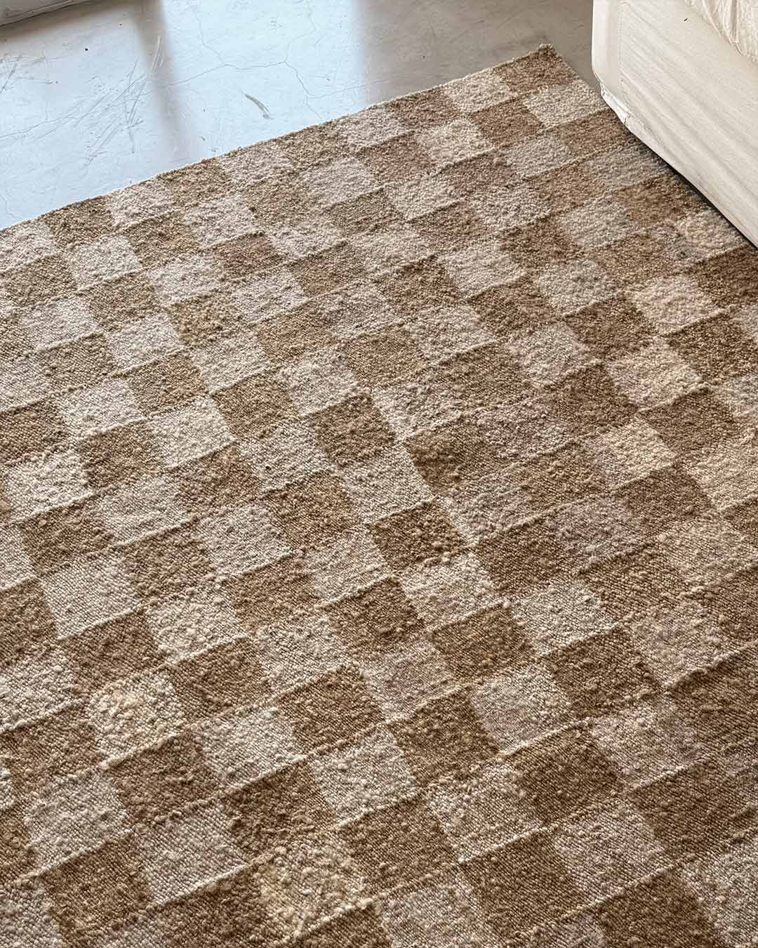 Checkered wool rug wood and sand tones beside light sofa