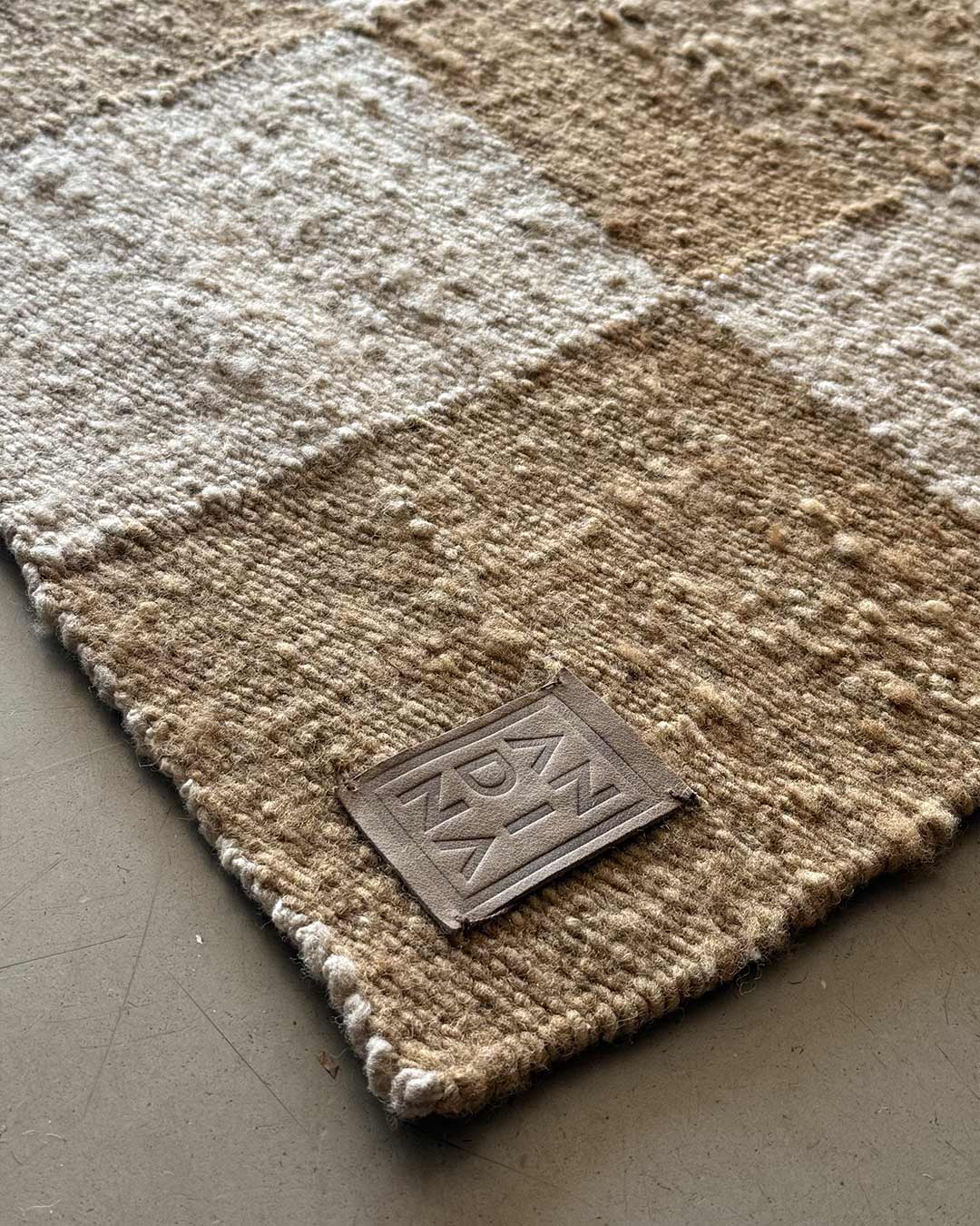 Close-up of wood and sand checkered wool rug with ANDINA label