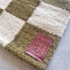 Close-up of the Natural & Moss Checkered Runner rug showing a moss green and white checkered pattern with a brown ANDINA leather tag.