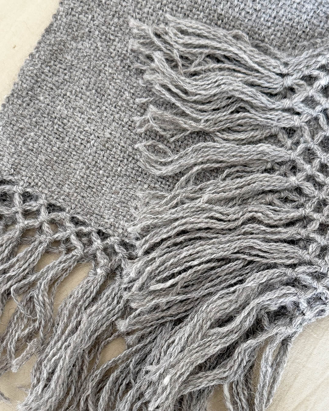 Detail of ANDINA’s Ash llama throw showing interlaced fringe and woven gray fabric.