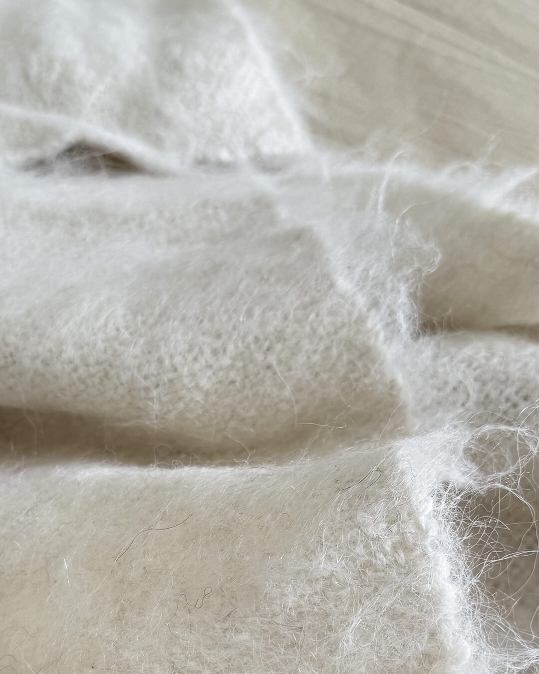 Detailed shot of ANDINA’s brushed llama throw in Natural White, highlighting its airy undyed fibers.