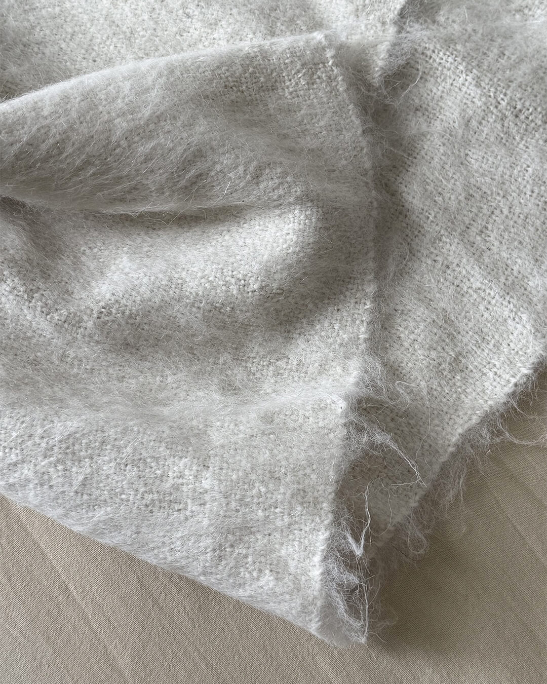 ANDINA’s Natural White brushed llama throw folded gently showing fluffy wool texture.