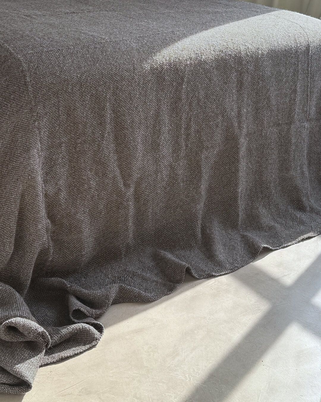 Frazada de llama en tono Sombra Gris de ANDINA sobre una cama minimalista con textiles superpuestos y luz cálida.