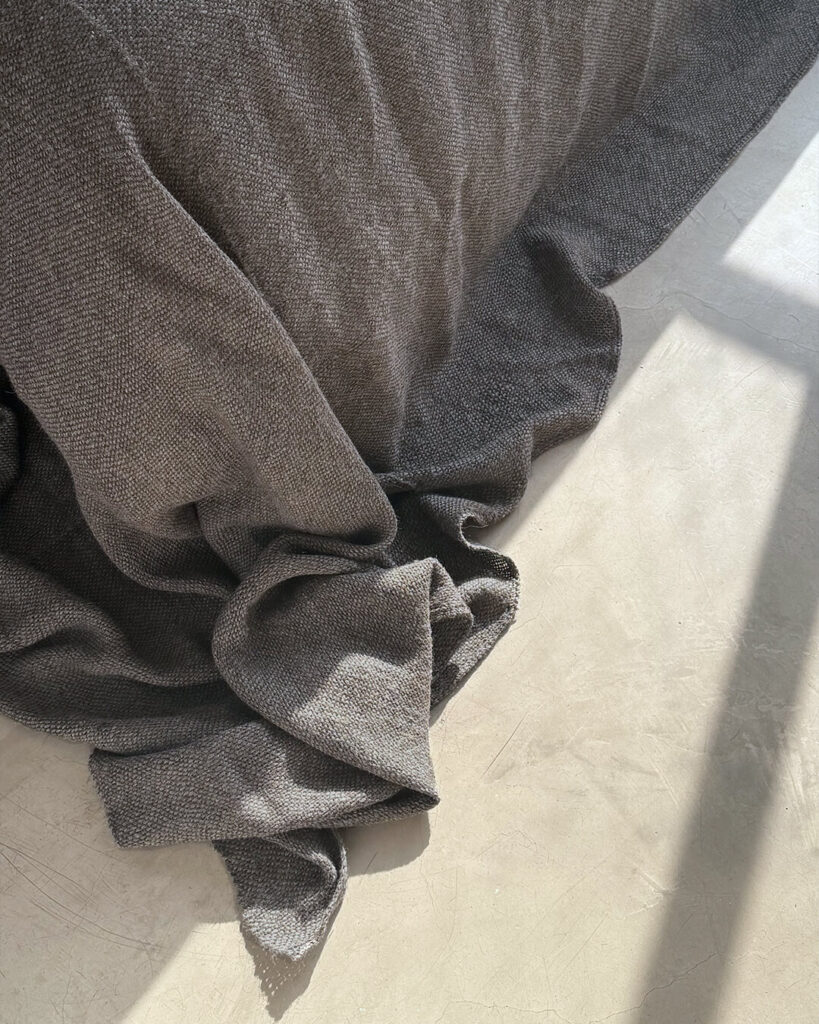 Llama bed quilt shadow gray draped over bed with soft natural light — handwoven undyed llama fiber