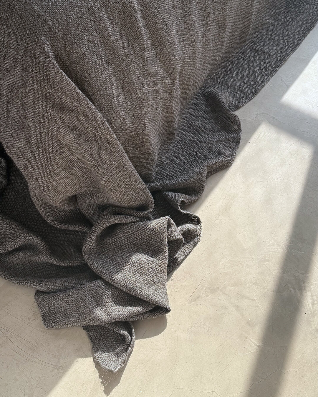 Frazada de llama sin teñir en tono Sombra Gris de ANDINA, apoyada sobre una cama con luz natural suave.