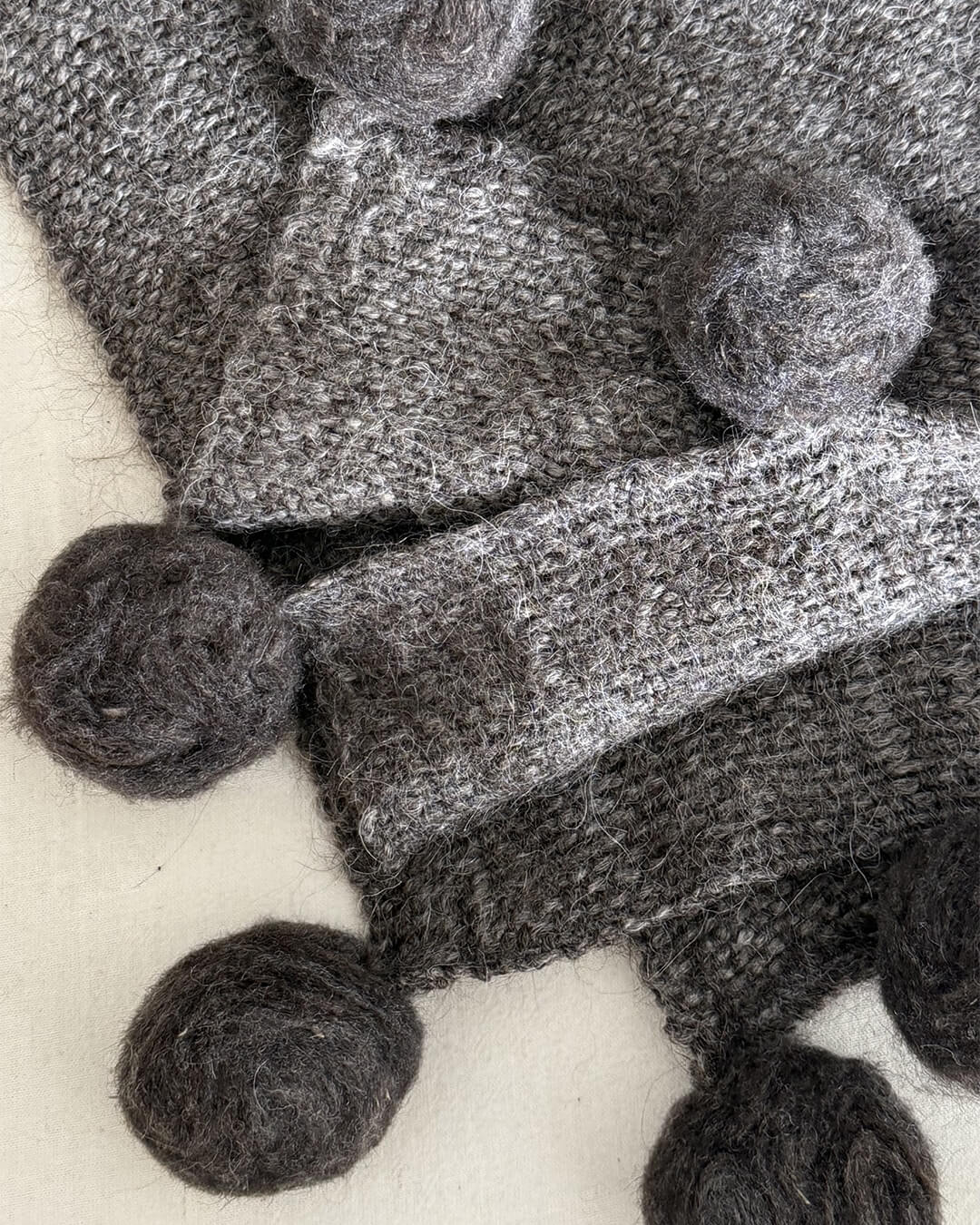 ANDINA’s Shadow llama throw with hand-felted pom poms in dark gray tones.
