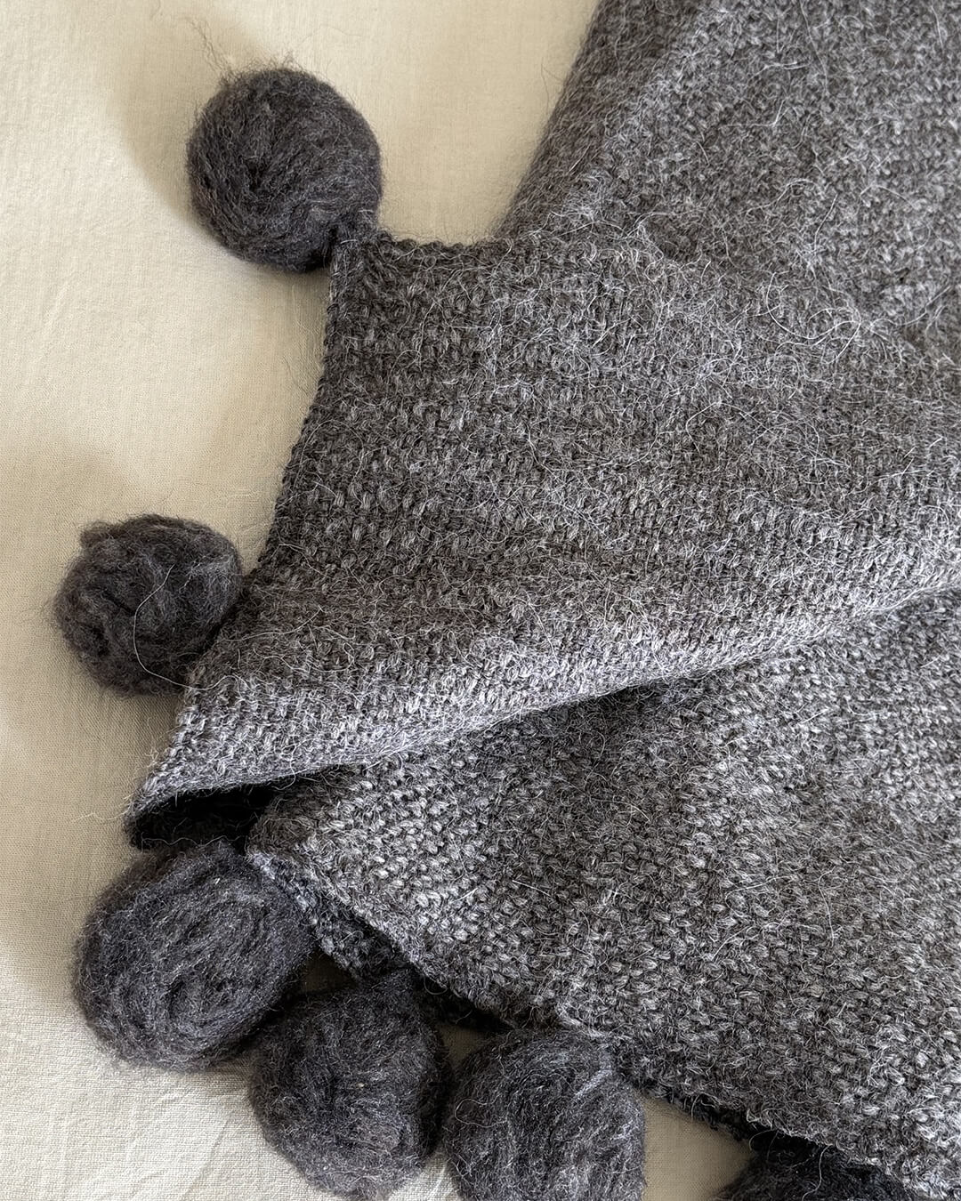 Close-up of ANDINA’s Shadow llama throw showing woven texture and soft pom poms.