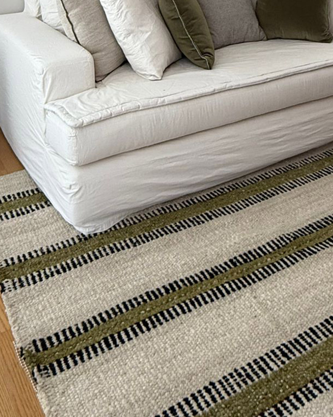 Yunga rug in natural, moss, and black tones, handwoven wool rug styled under a sofa.