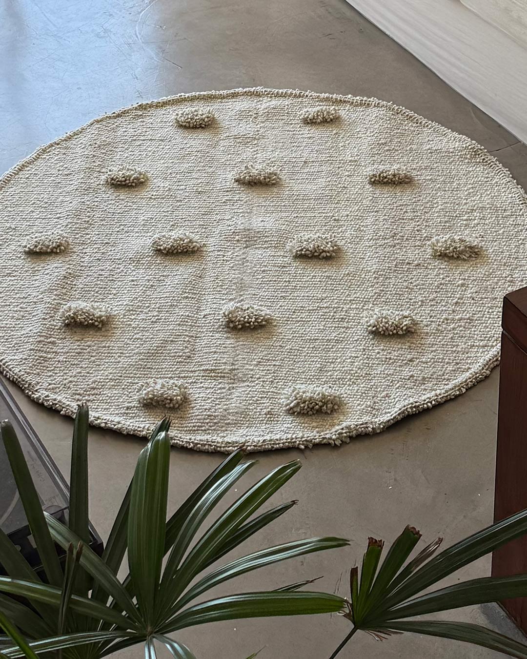 Top view of a round pom pom rug in natural wool with evenly spaced textured accents.