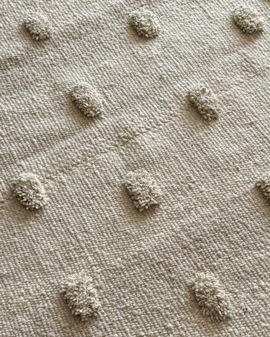 Close-up detail of natural wool pom poms on a handwoven round rug.
