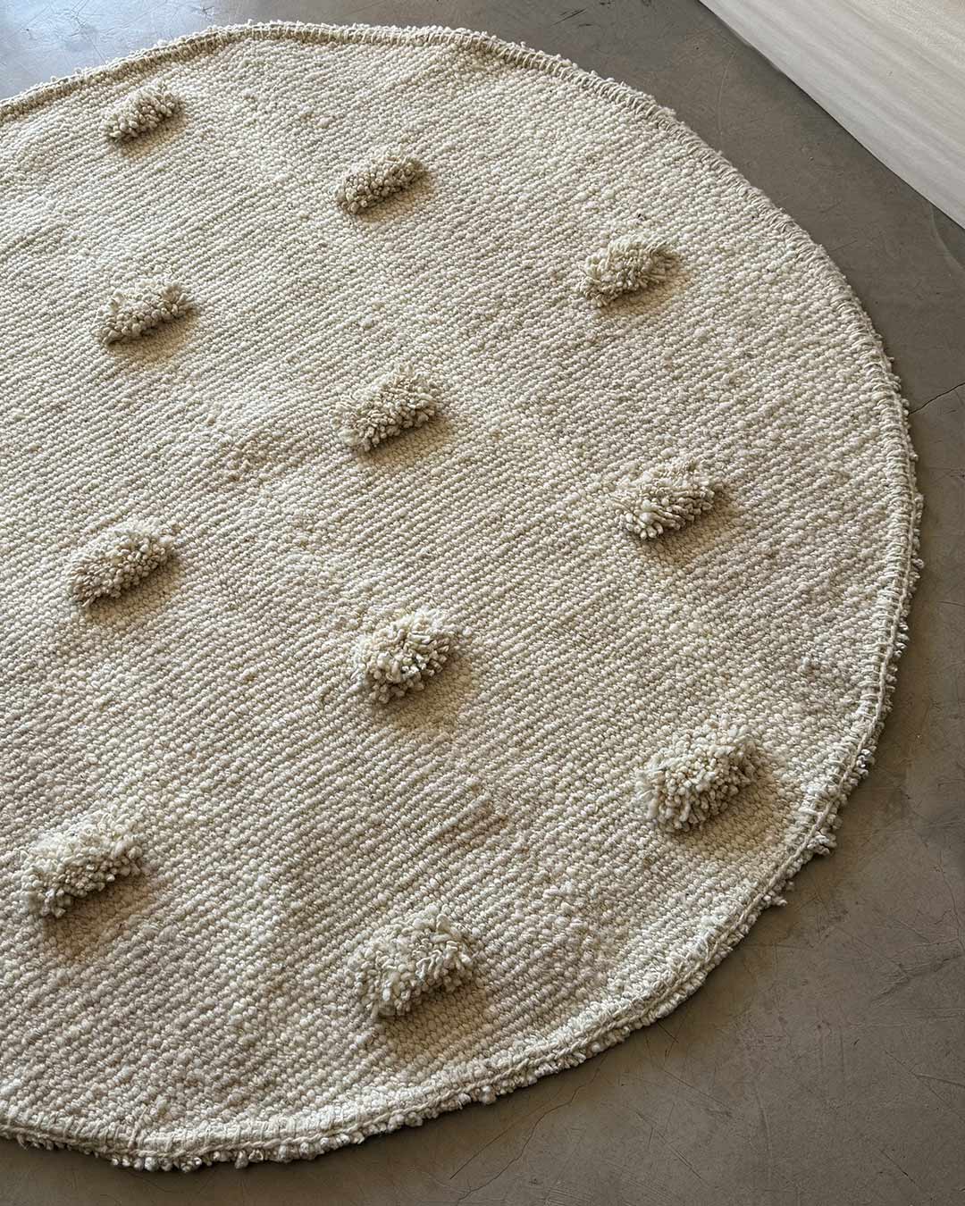Round Pom Pom rug in natural wool, handwoven in Argentina, shown in a minimalist interior.