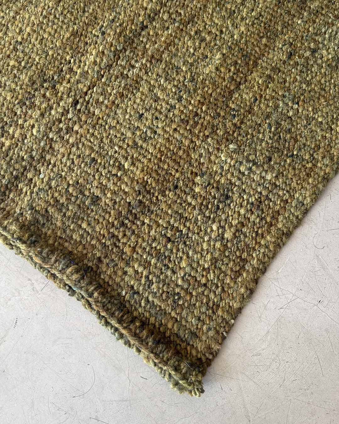 Corner detail of solid moss wool rug on concrete floor