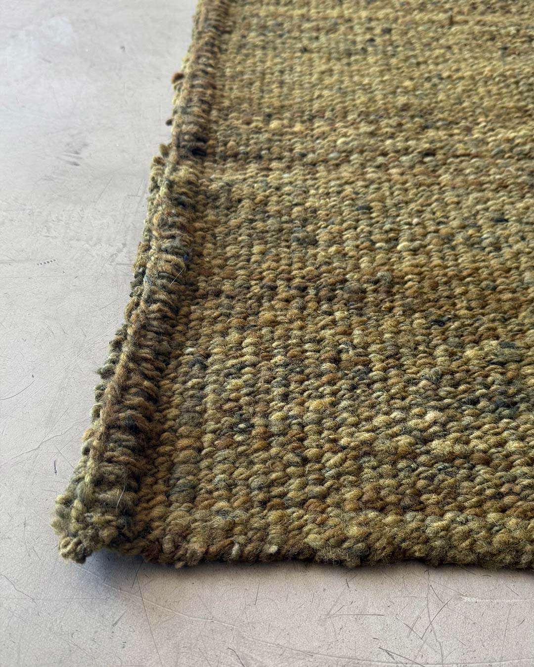 Edge detail of solid moss wool rug handwoven texture