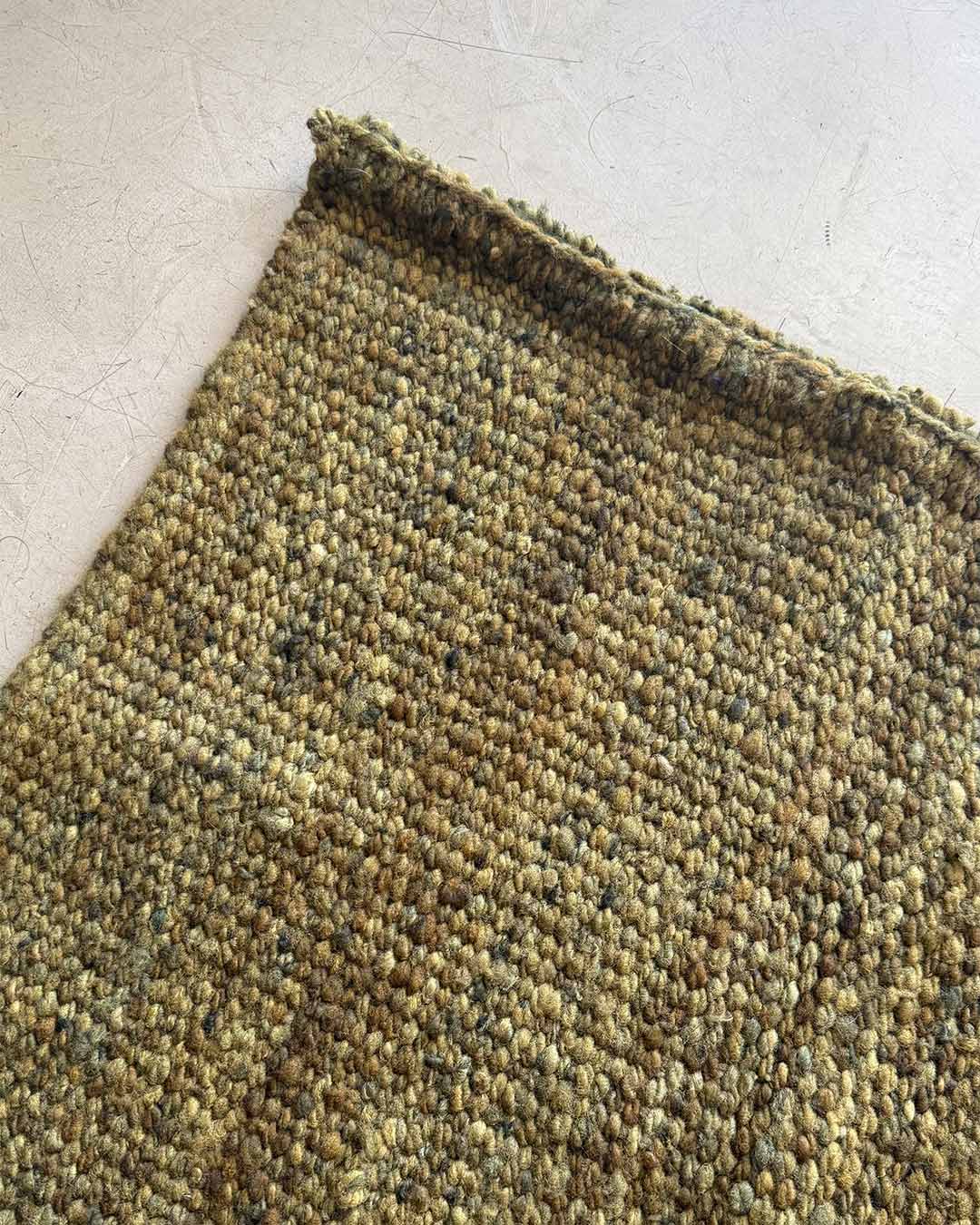 Top corner detail of solid moss handwoven wool rug