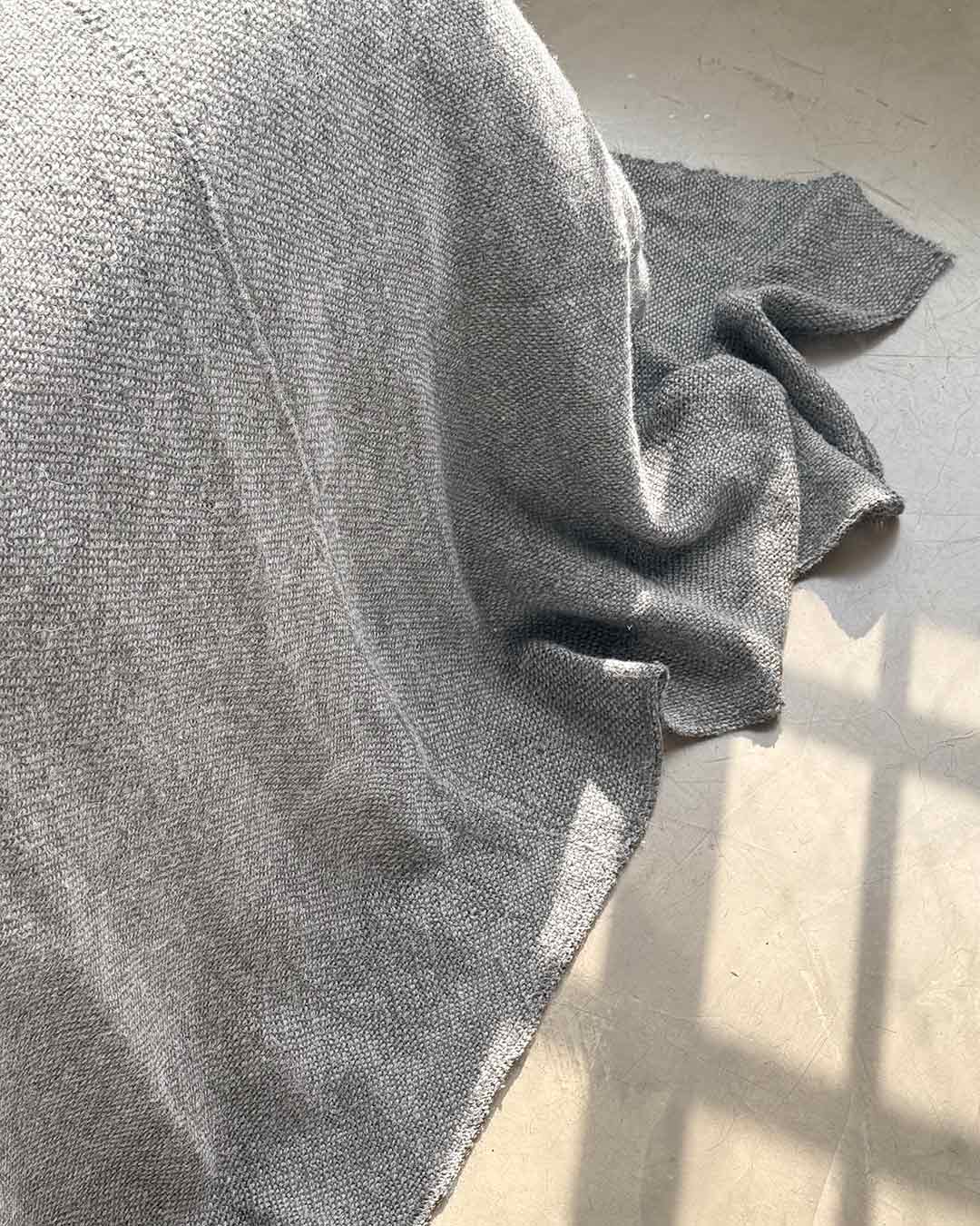 Cubrecama de llama puro ceniza gris claro sobre cama con luz natural y textiles en capas