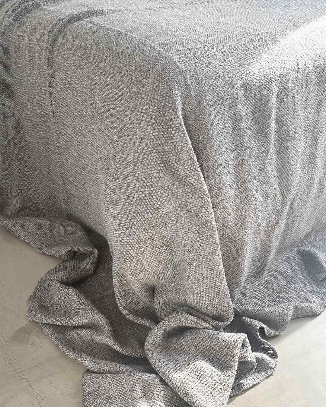 Close-up of ash gray llama fiber weave showing pale cool texture of undyed handwoven bed quilt