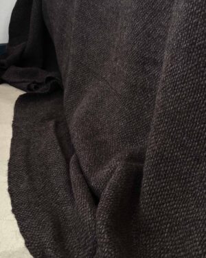 Handwoven black llama bed quilt on concrete floor showing full weave structure
