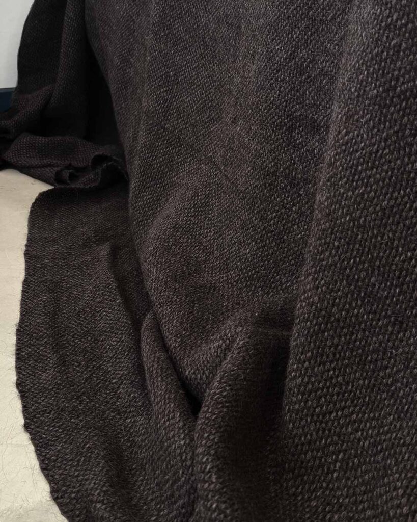 Handwoven black llama bed quilt on concrete floor showing full weave structure