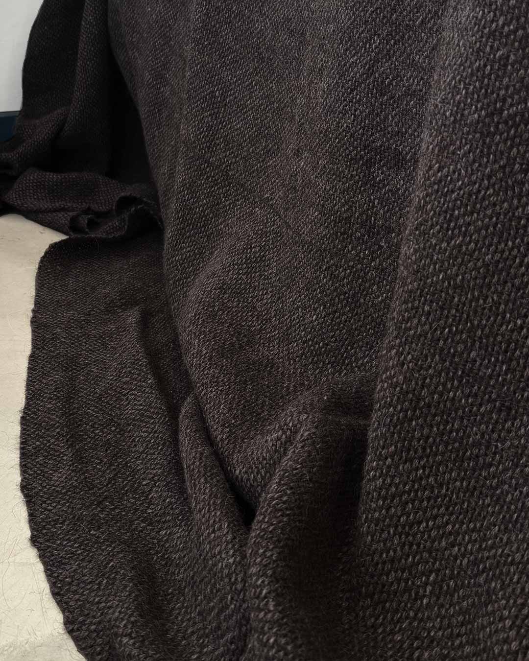 Handwoven black llama bed quilt on concrete floor showing full weave structure