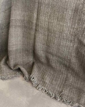 Llama bed quilt oat pale warm beige on concrete floor showing full handwoven structure and fringe