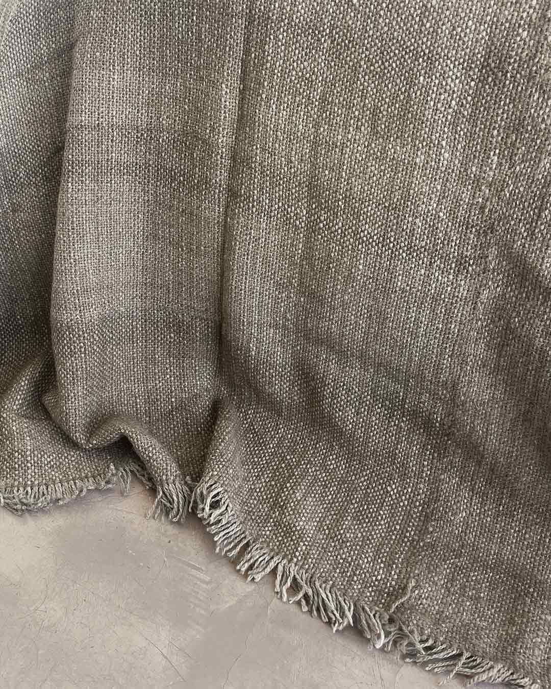 Llama bed quilt oat pale warm beige on concrete floor showing full handwoven structure and fringe