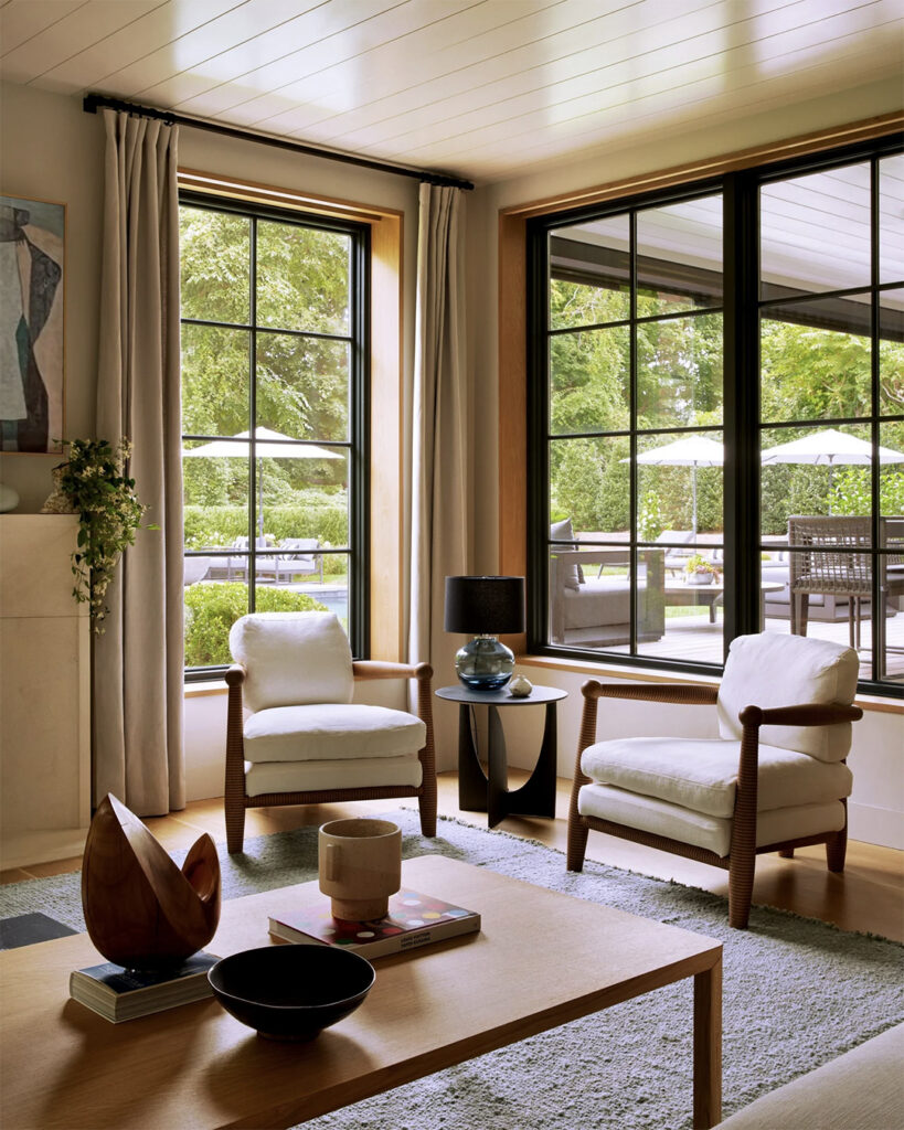 Blue gray wool rug beneath two white linen armchairs by a bank of windows