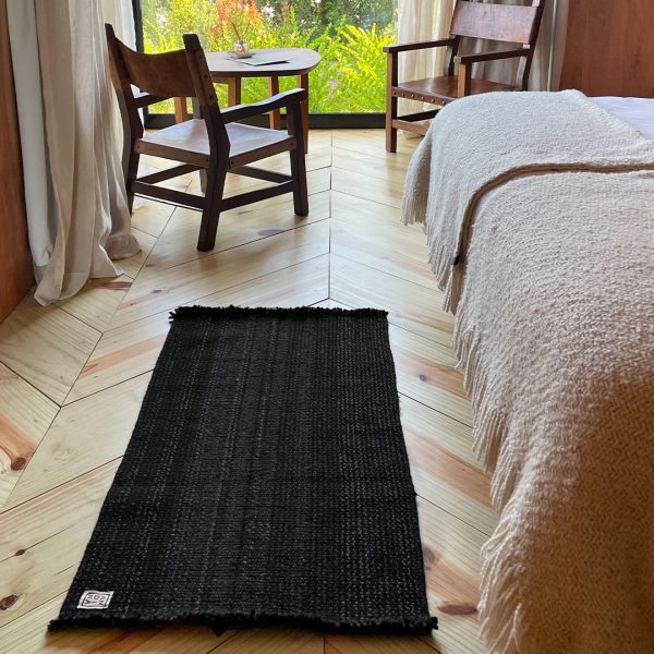 ANDINA’s Solid Runner Rug in black undyed wool placed beside a bed in a natural wood interior.